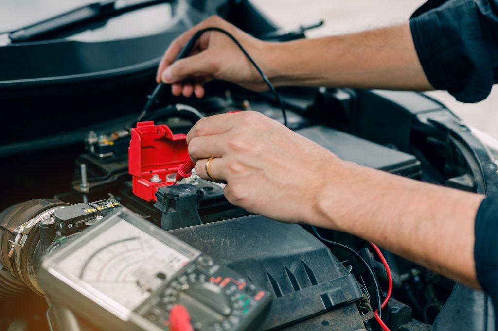 Car mechanic is using the car battery meter to measure various values and analyze it.